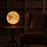 The Andorra antique ocean globe illuminated on a small side table next to a leather armchair in a dim library setting.