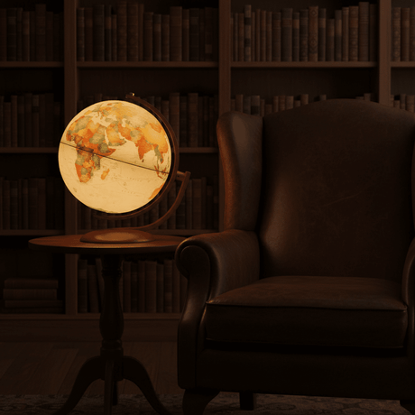 The Andorra antique ocean globe illuminated on a small side table next to a leather armchair in a dim library setting.